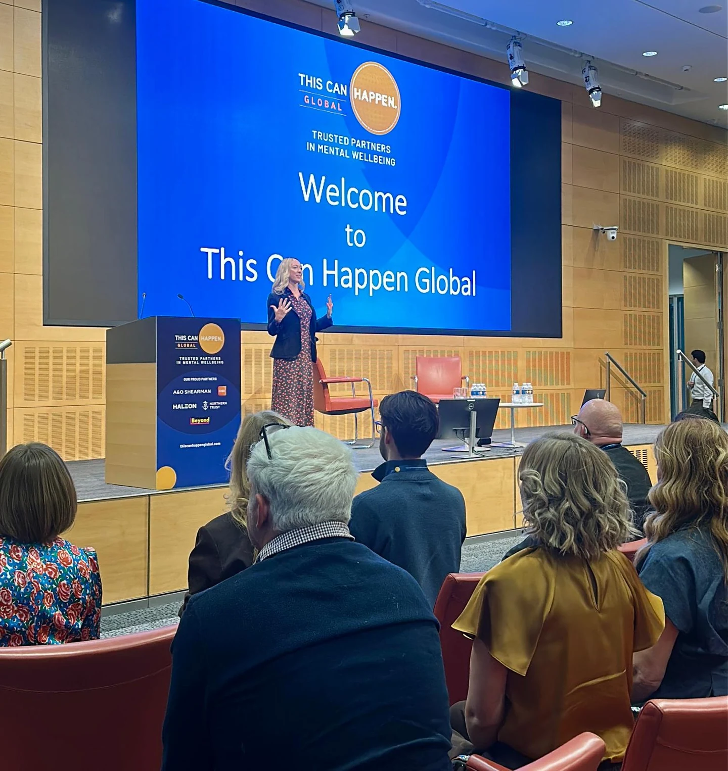Catherine speaking on stage at This Can Happen Global with an audience